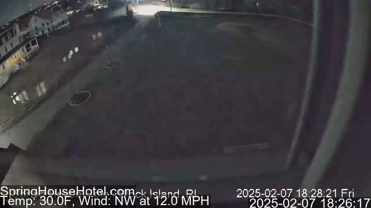 A nighttime, overhead view of a mostly empty parking lot and street next to some buildings, with a northwest wind at 12 mph and a temperature of 30 degrees Fahrenheit.