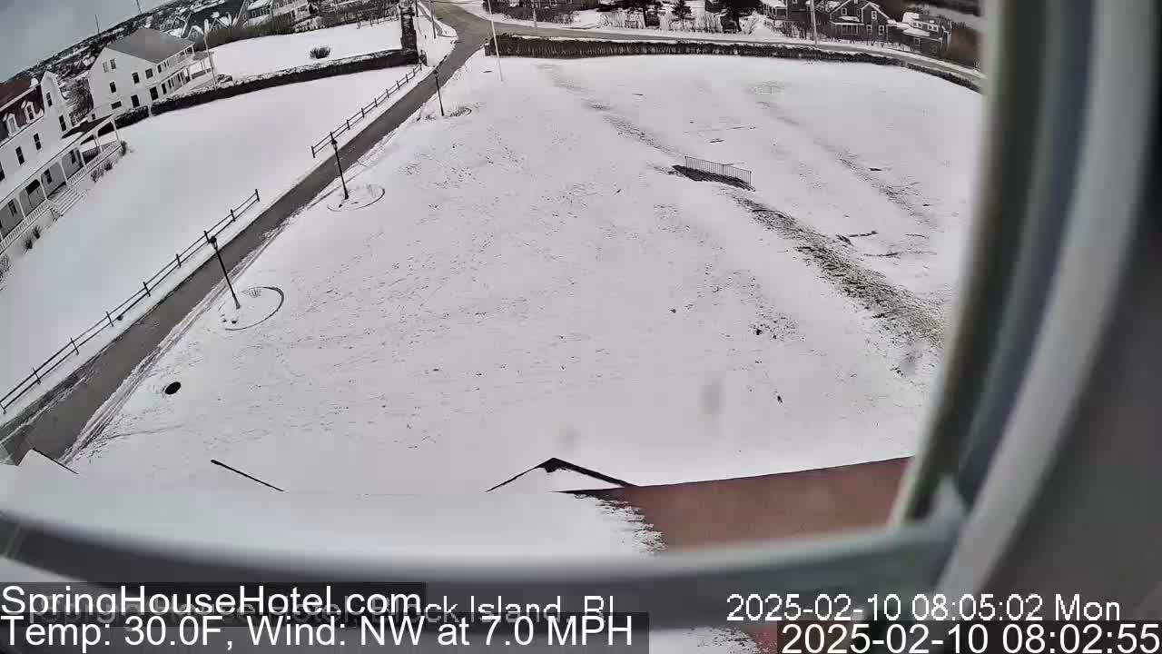 A snow-covered ground with a road and buildings in the background, under a cloudy sky with a northwest wind at 7.0 mph and a temperature of 30 degrees Fahrenheit.