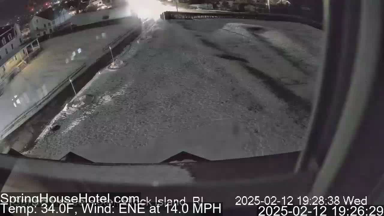 A snow-covered nighttime scene shows a building and a large expanse of ground under a dark sky, with a wind from the east-northeast at 14 mph and a temperature of 34°F.