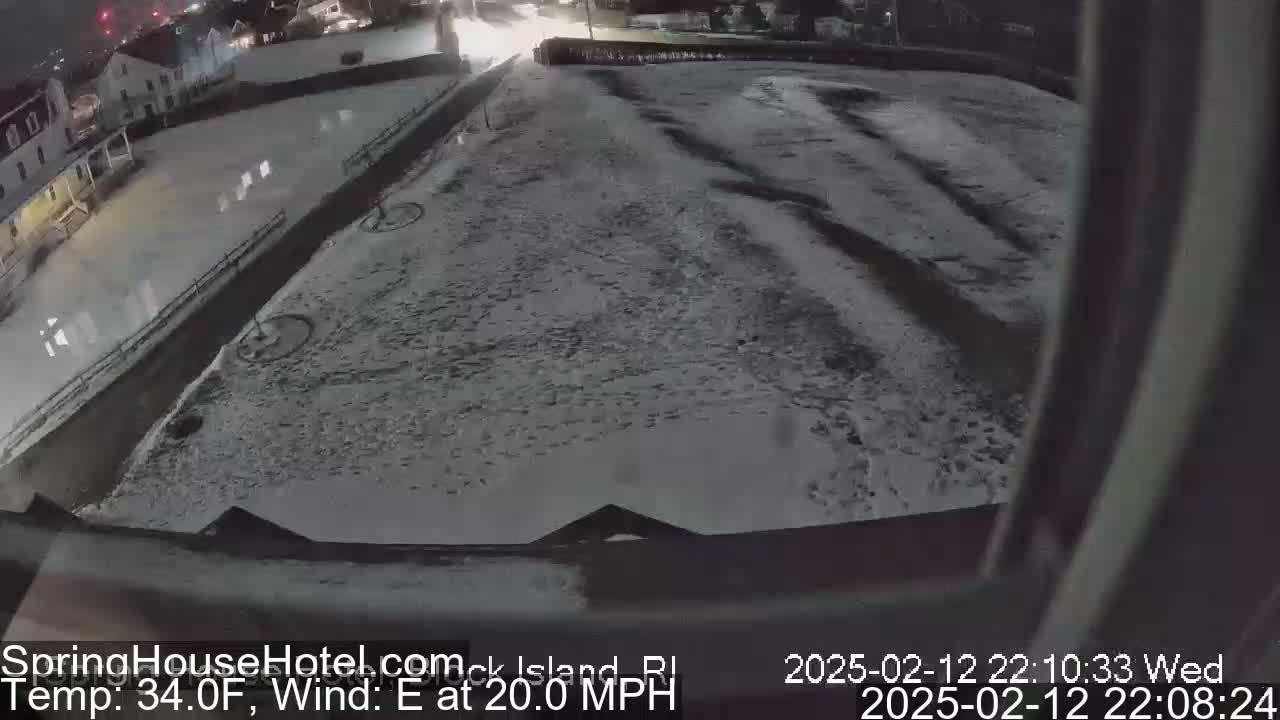 A snow-covered parking lot and street are visible at night, with a building in the background, under an east wind blowing at 20 mph and a temperature of 34°F.