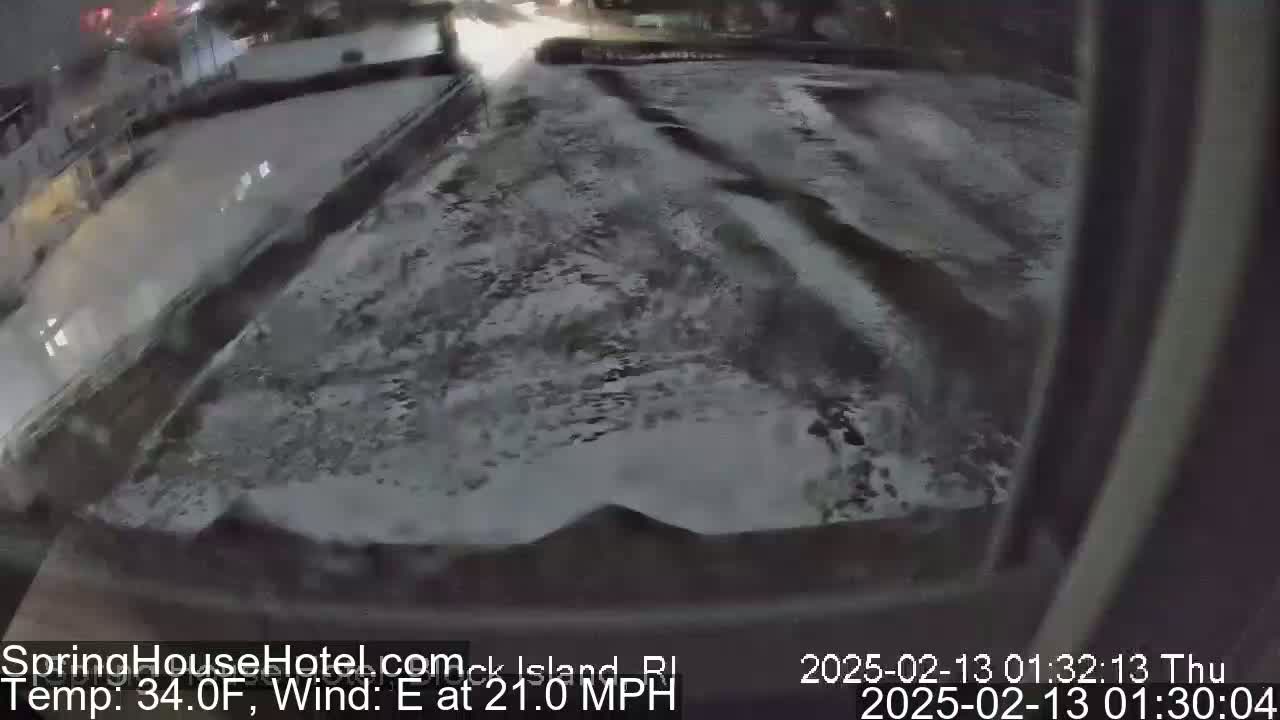 A snow-covered parking lot and roadway are visible from a window at night, with an easterly wind blowing at 21 mph and a temperature of 34°F.