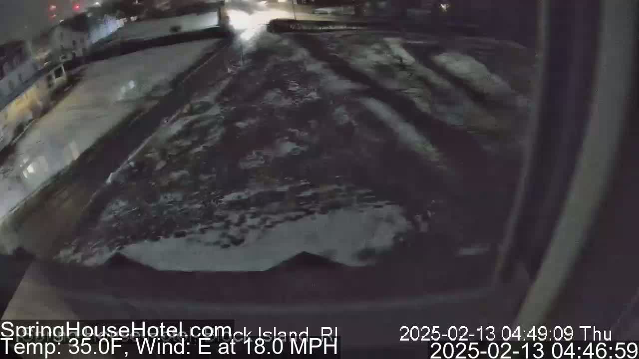 A nighttime, snowy scene shows a mostly empty street with some snow accumulation on the ground and an 18 mph easterly wind.