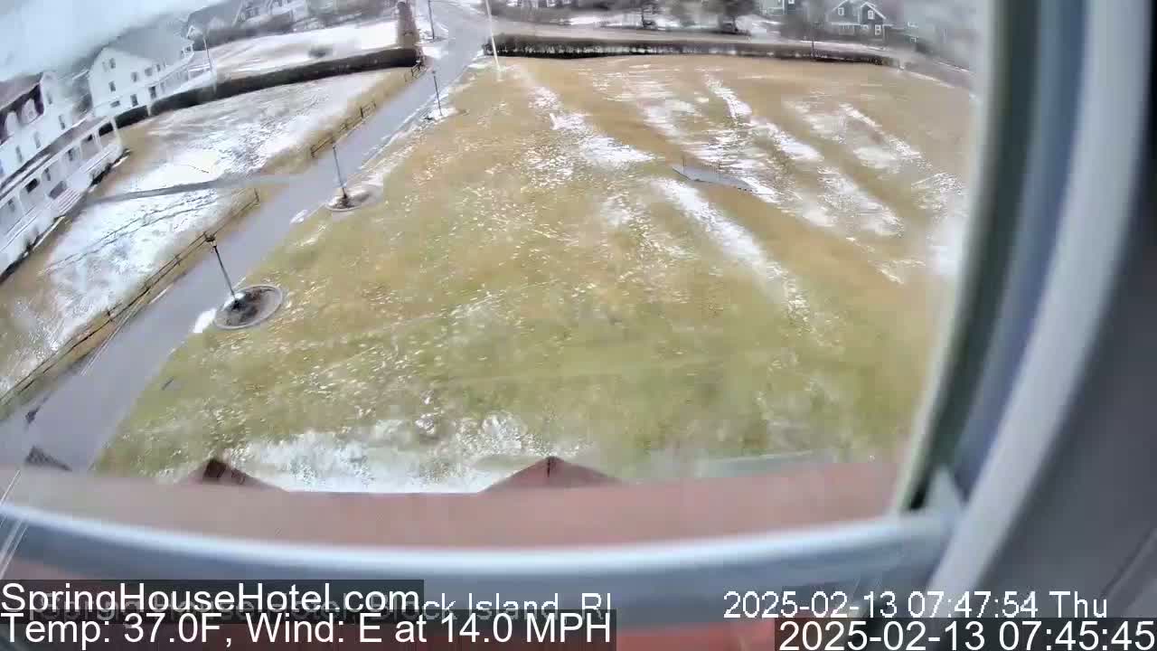 A view from a window shows a grassy area with patches of snow, partially flooded by water and experiencing strong east winds at 37 degrees Fahrenheit.
