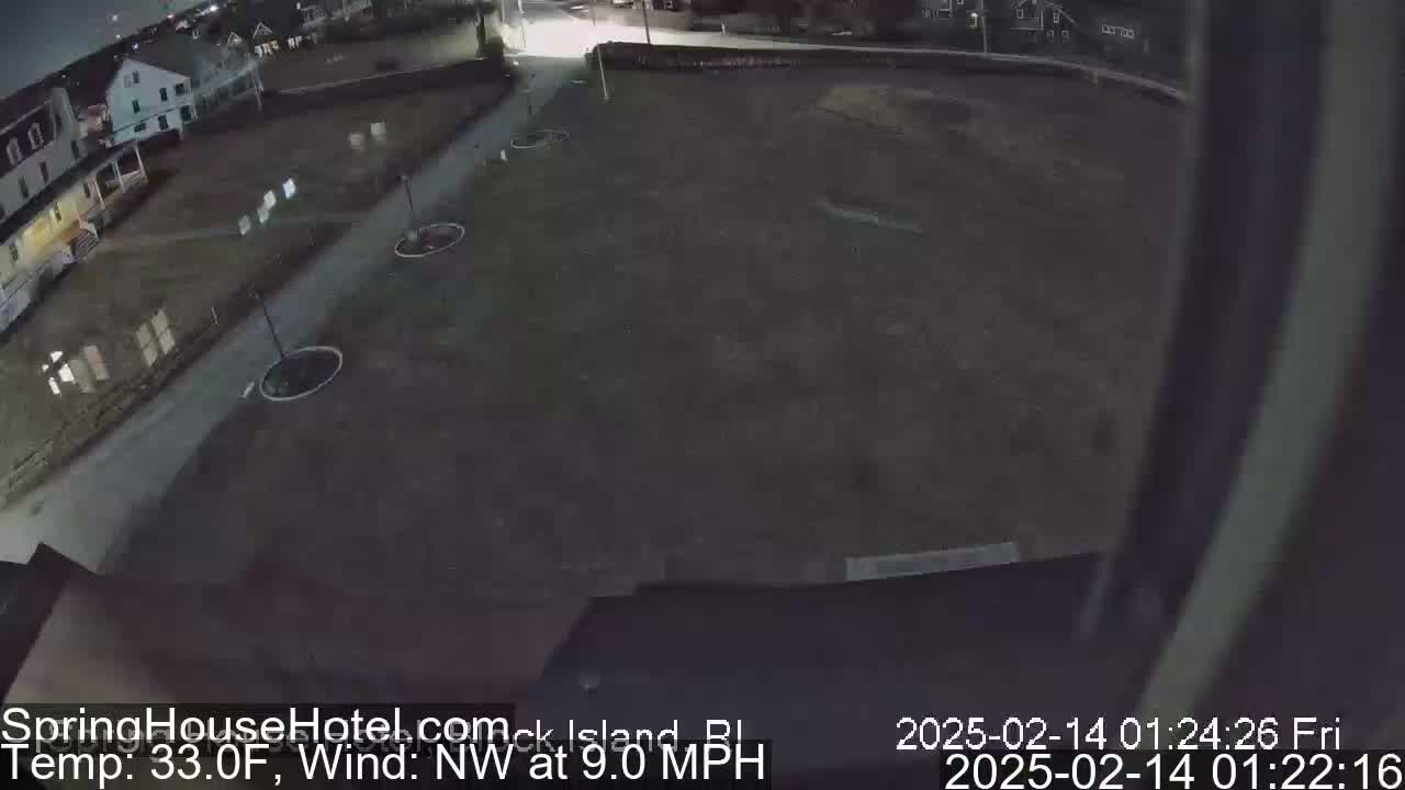 A nighttime view of a dark, empty paved area near some buildings, with a northwest wind at 9 mph and a temperature of 33 degrees Fahrenheit.
