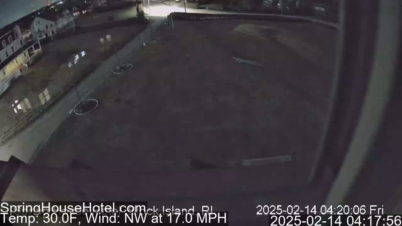 A nighttime, outdoor view of a dark, mostly empty paved area near a building, with a northwest wind blowing at 17 miles per hour and a temperature of 30 degrees Fahrenheit.