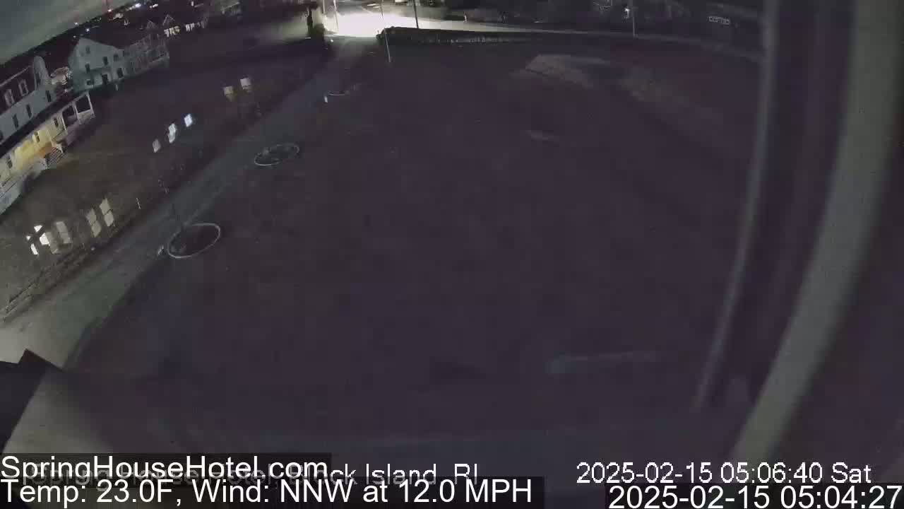 A nighttime, low-light view of a mostly empty parking lot next to a building, with a northwest wind at 12 miles per hour and a temperature of 23 degrees Fahrenheit.