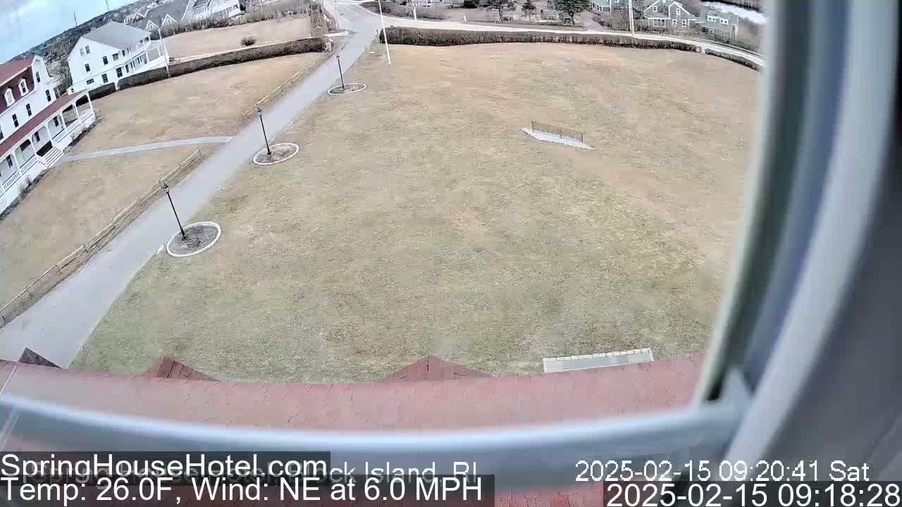 A view from a window shows a large grassy area with a paved pathway, buildings in the background, and a northeast wind at 6.0 mph with a temperature of 26.0°F.