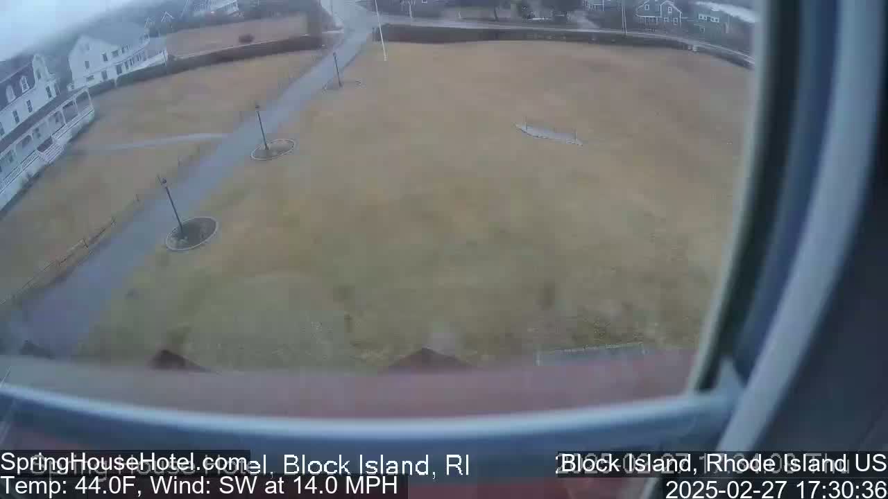 A high-angle view shows a large, flat, brown expanse of grass with pathways and lampposts, bordered by buildings under an overcast sky with a southwest wind at 14 mph and a temperature of 44°F.