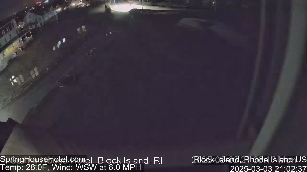 A nighttime, aerial view of a mostly empty parking lot next to buildings, with a wind of 8 mph from the west-southwest and a temperature of 28 degrees Fahrenheit.