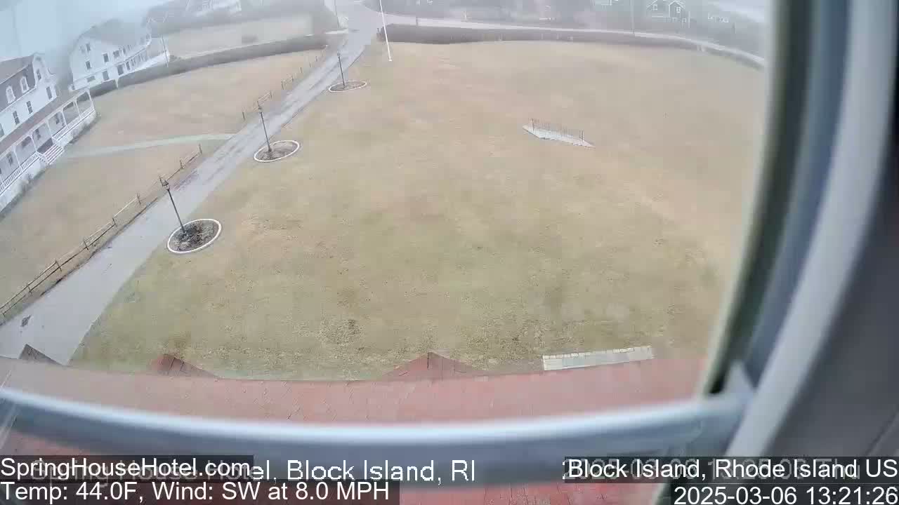 A view from a window shows a snow-covered grassy area with walkways and a building in the background, under overcast conditions.