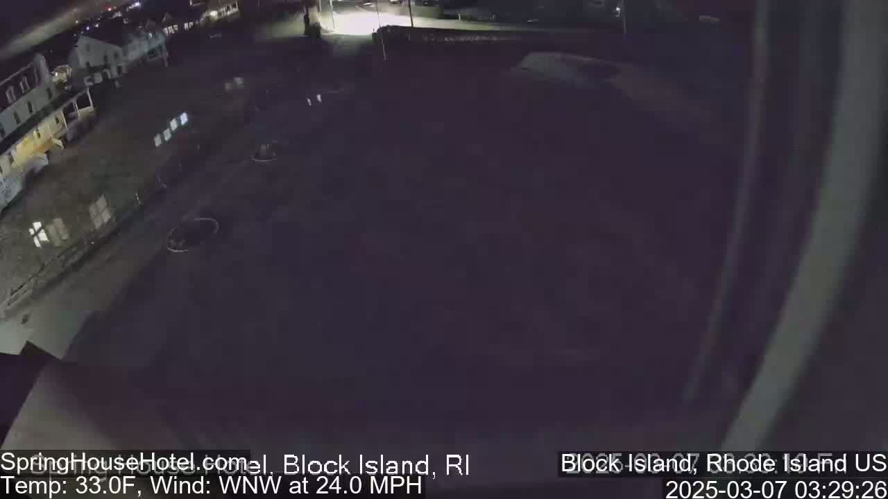 A nighttime, high-angle view of a dark parking lot and buildings, with a strong wind blowing.
