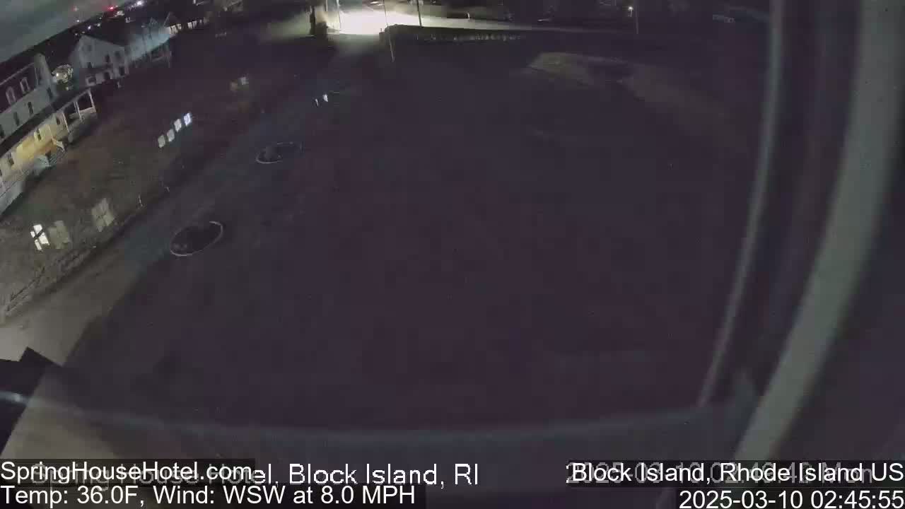 A nighttime, overhead view of a dark, mostly empty parking lot next to some buildings, with a southwest wind at 8 mph and a temperature of 36 degrees Fahrenheit.