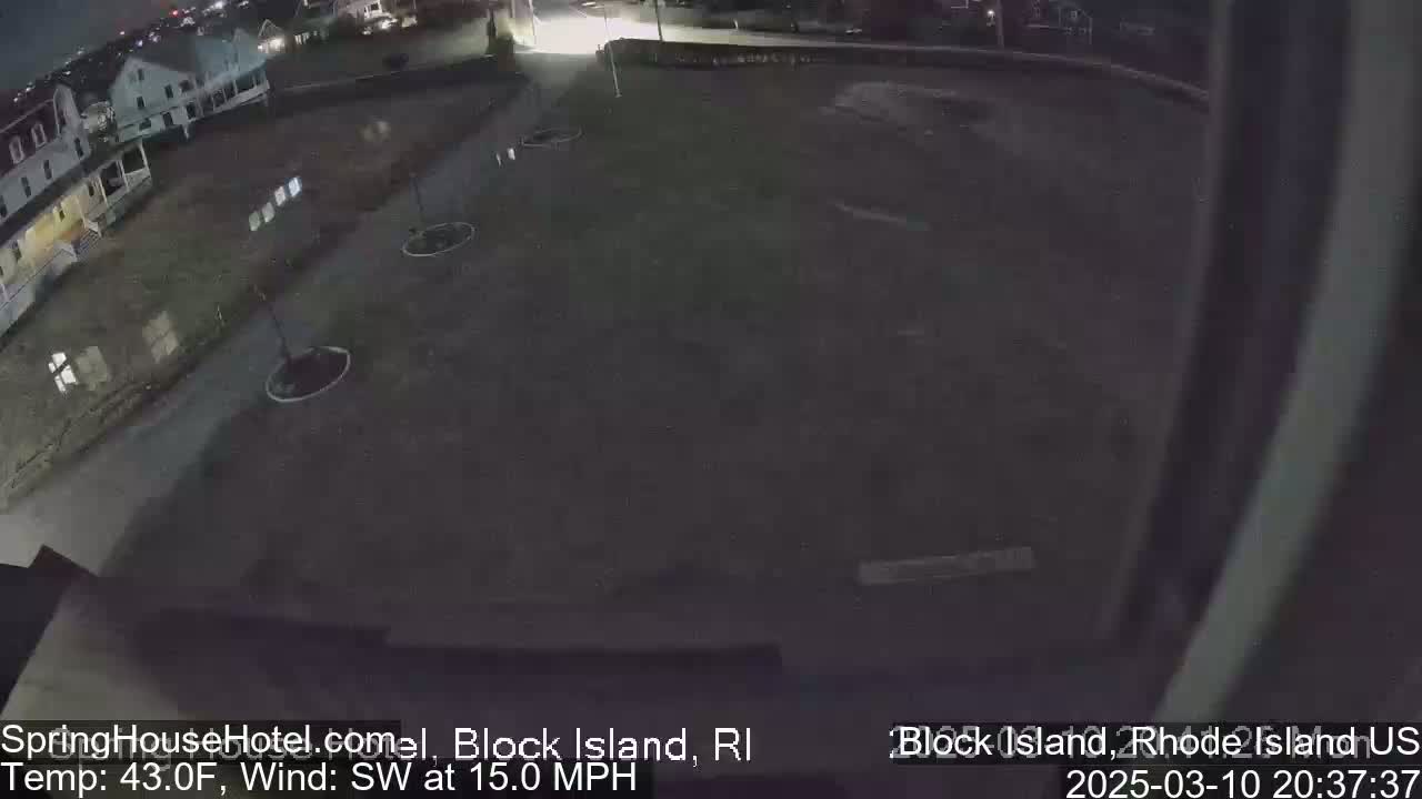 A nighttime, low-angle view of a mostly empty asphalt lot next to a building, under a dark sky with a southwest wind at 15 mph and a temperature of 43°F.