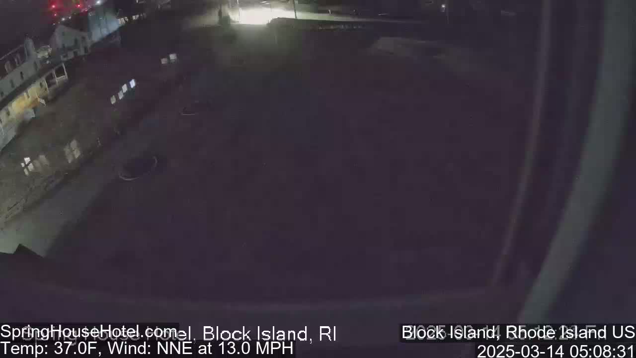 A nighttime, low-angle view of a dark, empty parking lot next to a building, with a north-northeast wind at 13 mph and a temperature of 37°F.