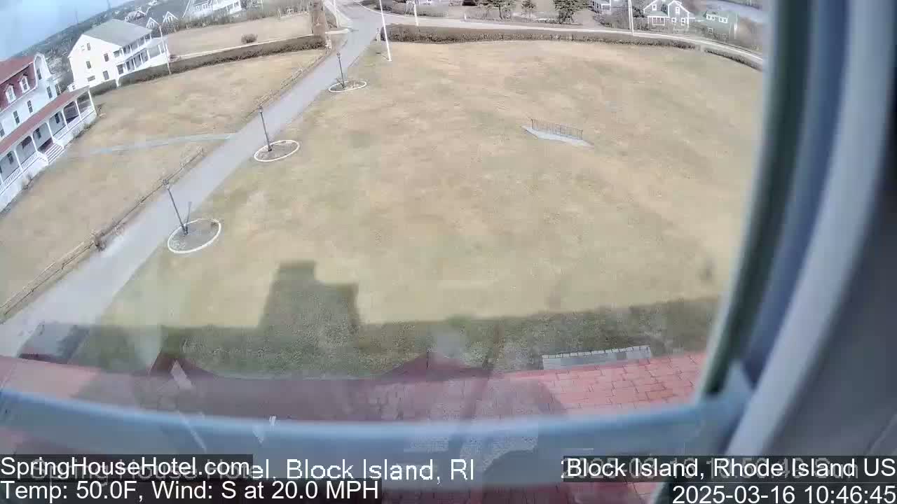 A view from a window shows a large, mostly brown grassy area with paved walkways, some buildings, and a 20 mph south wind in 50°F weather.