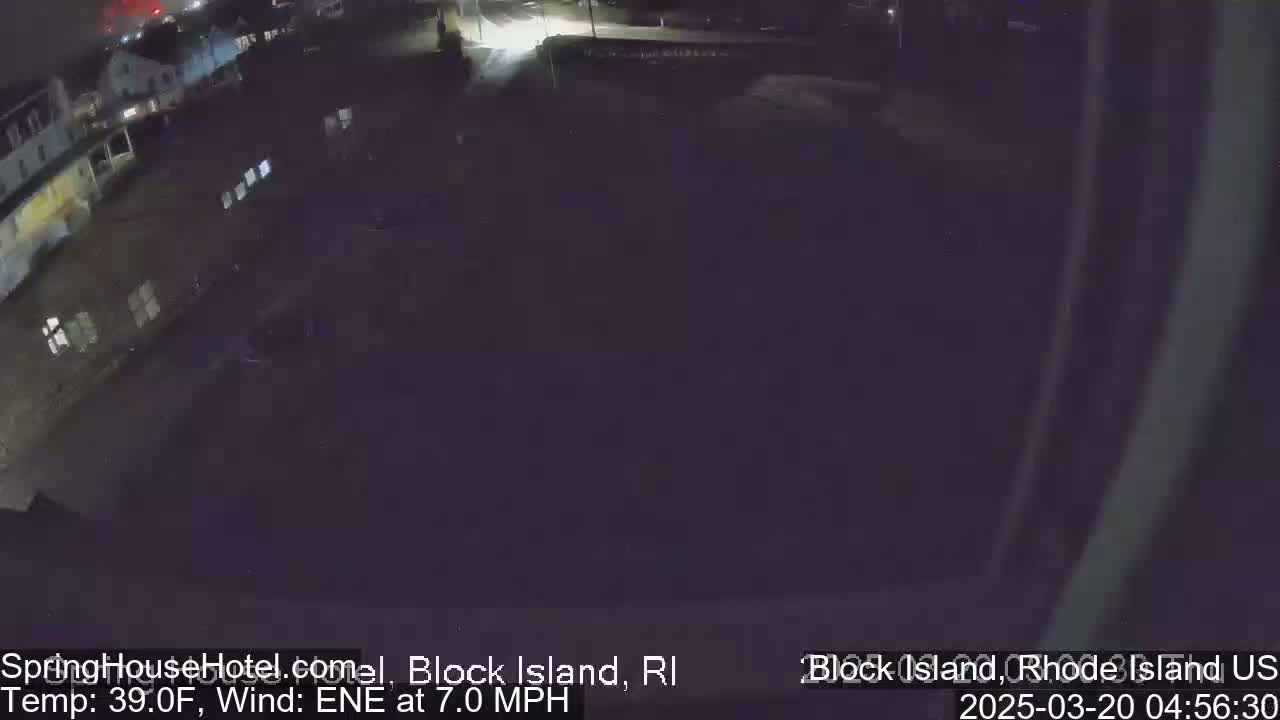 A dark, nighttime aerial view of a mostly empty parking lot next to buildings, with a 7 mph east-northeast wind and a temperature of 39°F.