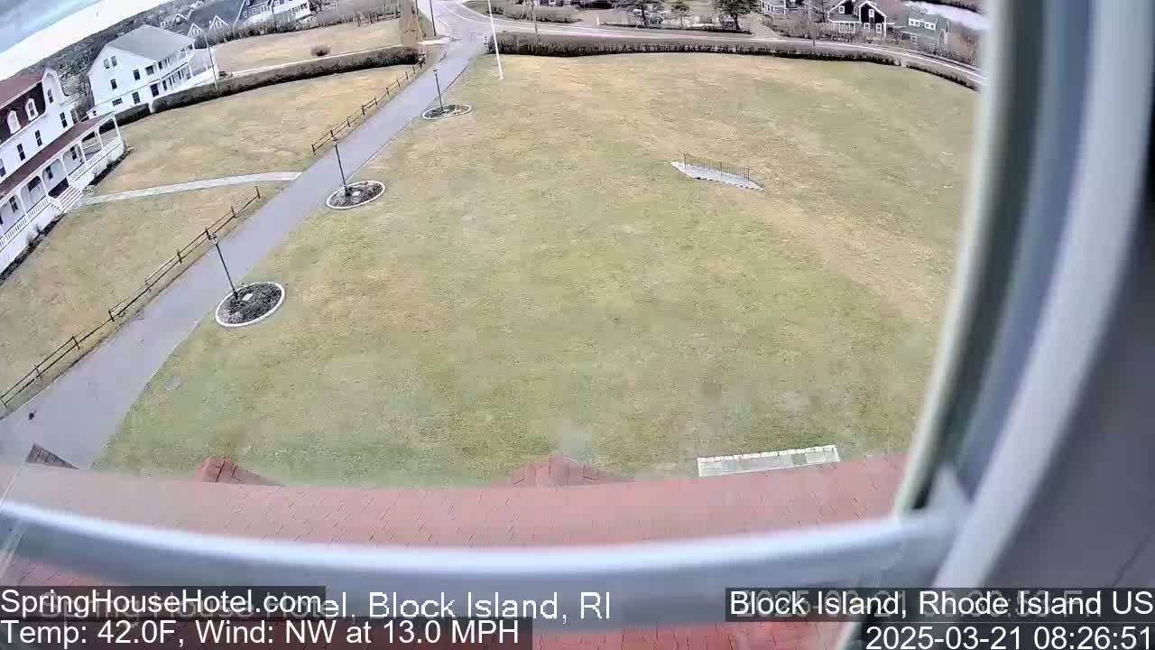 A view from a window shows a large grassy area with walkways, some buildings in the background, and a northwest wind at 13 mph with a temperature of 42 degrees Fahrenheit.
