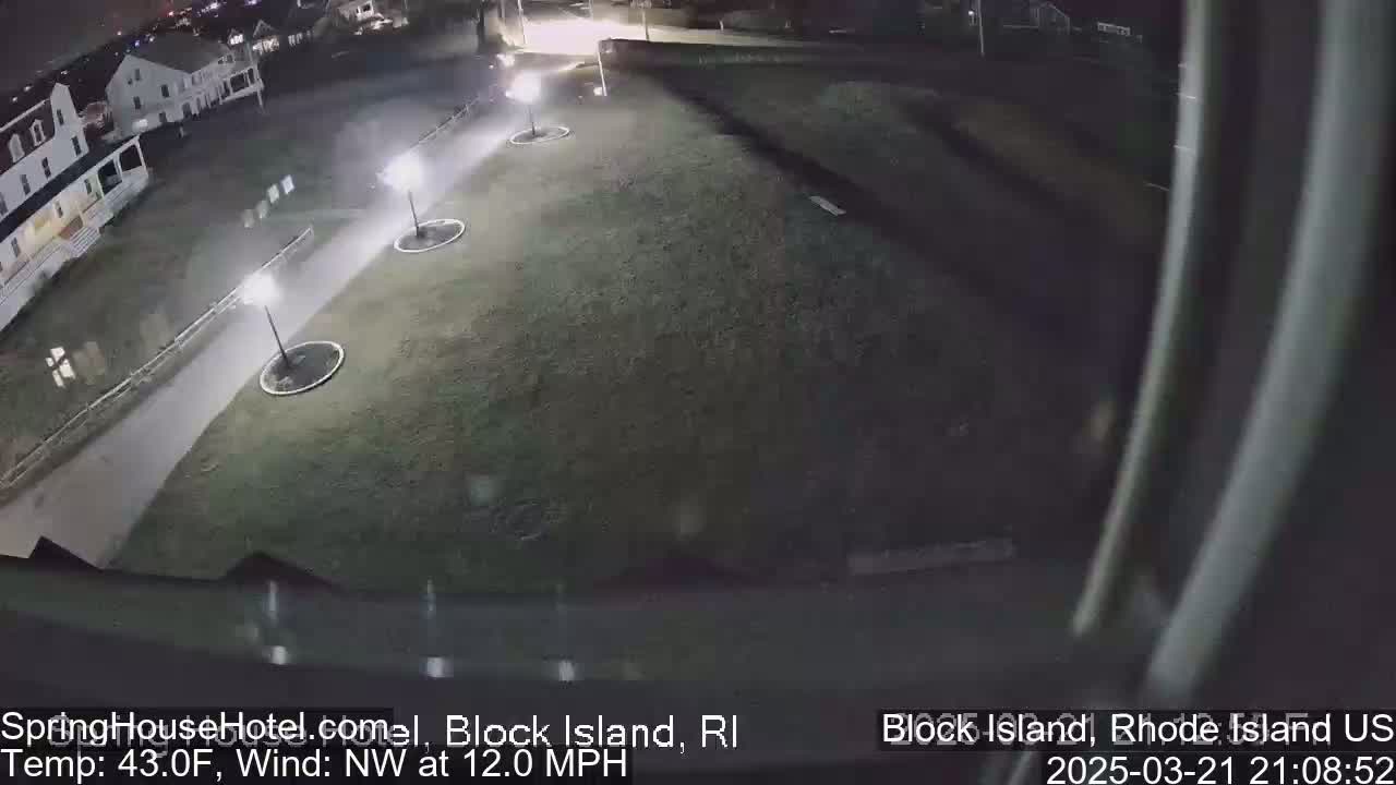 A nighttime view of a grassy area with a paved walkway, several light posts, and a building in the background, under a 43°F temperature with a northwest wind of 12 mph.