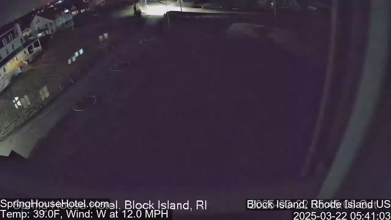 A nighttime, high-angle view of a mostly empty parking lot next to a building, with a 39°F temperature and a 12 mph west wind.