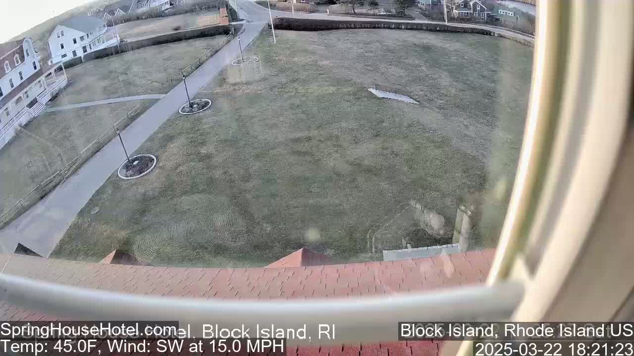 A high-angle view from a window shows a grassy area with walkways, buildings, and lampposts, under a partly cloudy sky with a southwest wind at 15 mph and a temperature of 45 degrees Fahrenheit.