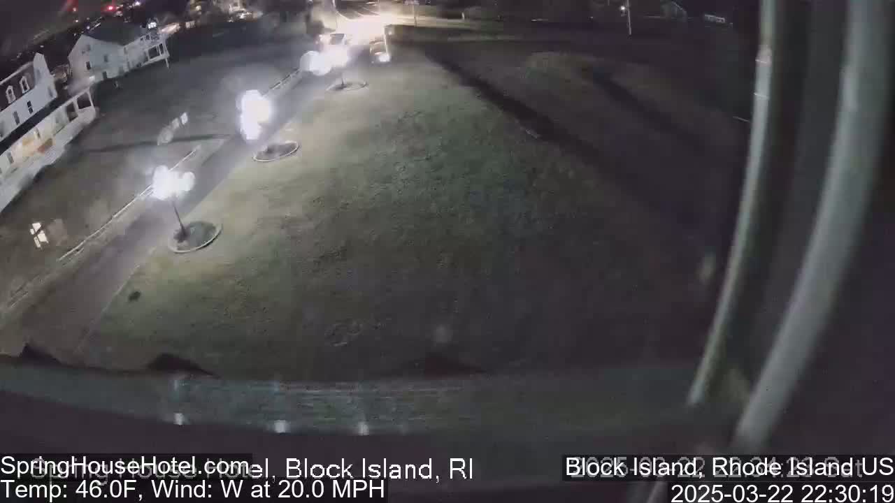 A nighttime, high-angle view of a parking lot and building with several lit streetlights, under windy conditions.