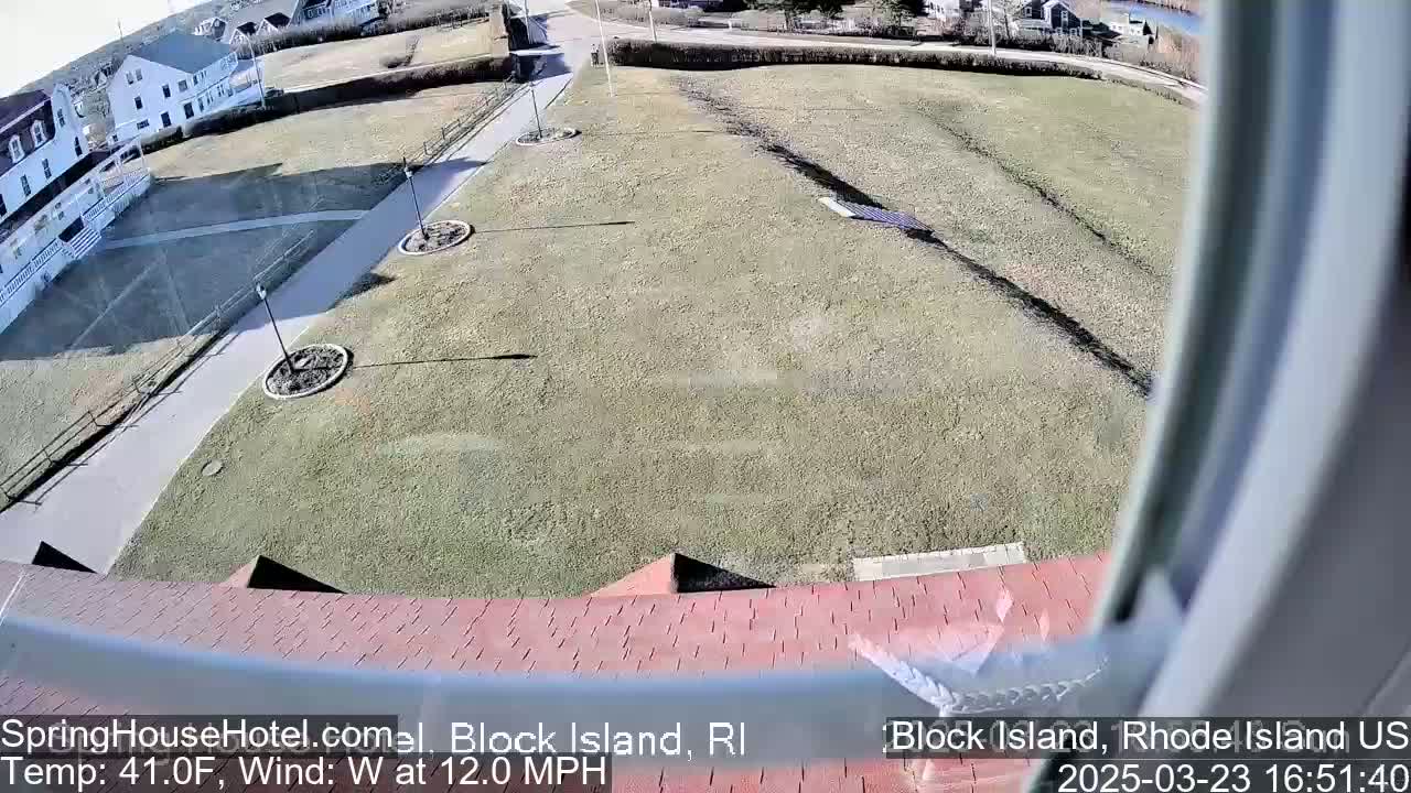 A view from a window shows a grassy area with pathways, landscaping, and buildings in the background on a sunny day with a 12 mph west wind and a temperature of 41°F.