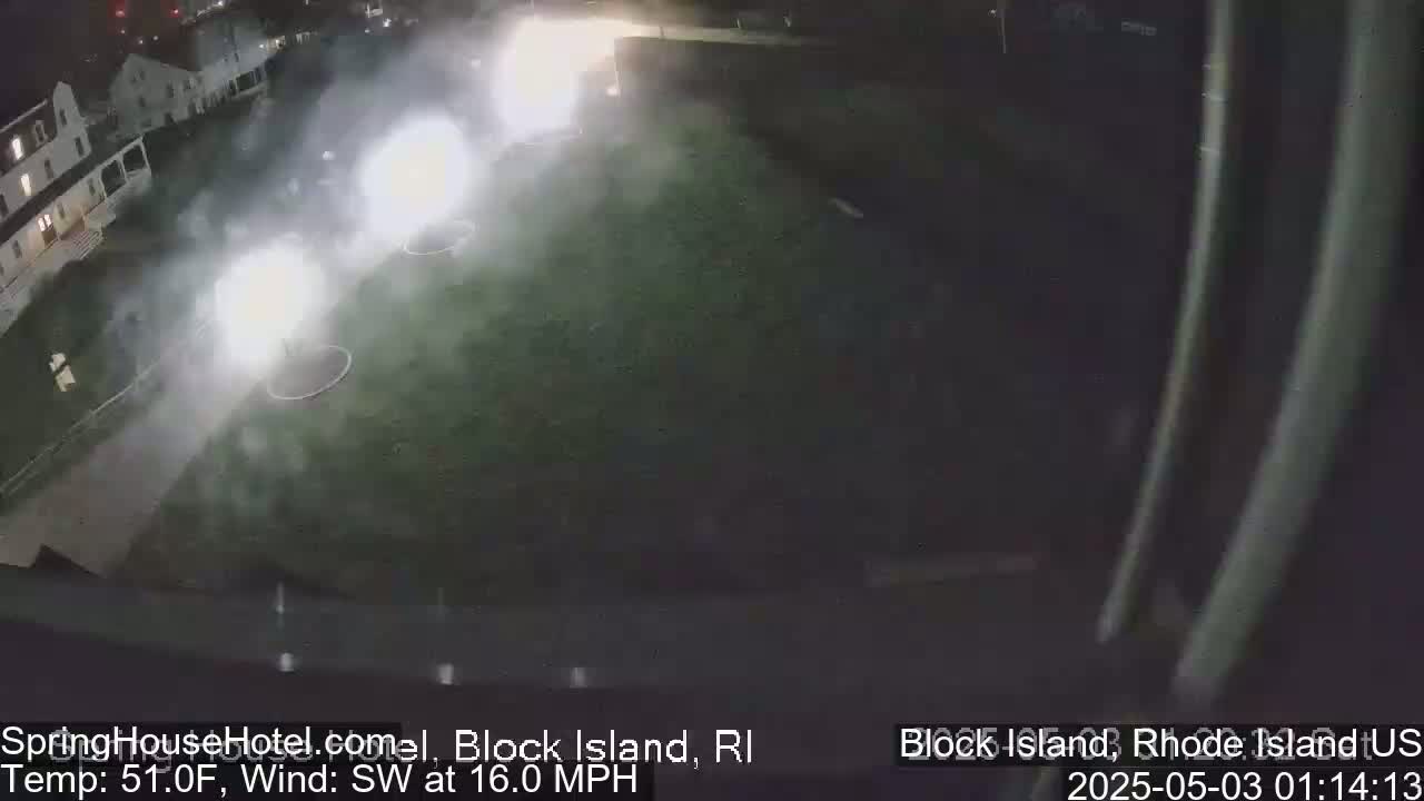 Several fireworks explode over a grassy area next to a building at night, with a southwest wind blowing at 16 mph and a temperature of 51°F.