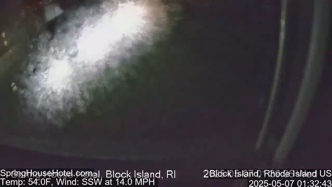 A nighttime, blurry image shows a bright light shining on a dark, possibly watery surface with a 14 mph south-southwesterly wind and a temperature of 54°F.