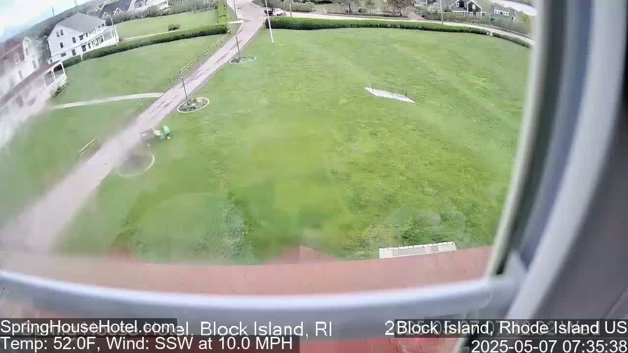 A high-angle view shows a lawn being mowed by a riding lawnmower on a windy day.