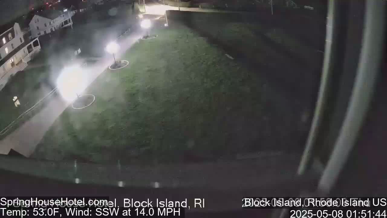 A nighttime, high-angle view shows a brightly lit area of grass near a building, with a hazy or foggy atmosphere and a 14 mph wind from the southwest.