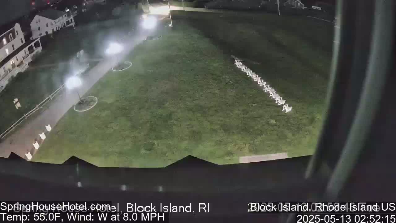 A nighttime, overhead view of a grassy area with a row of chairs and a paved walkway leading to a building, under partly cloudy skies with an 8 mph west wind and a temperature of 55°F.