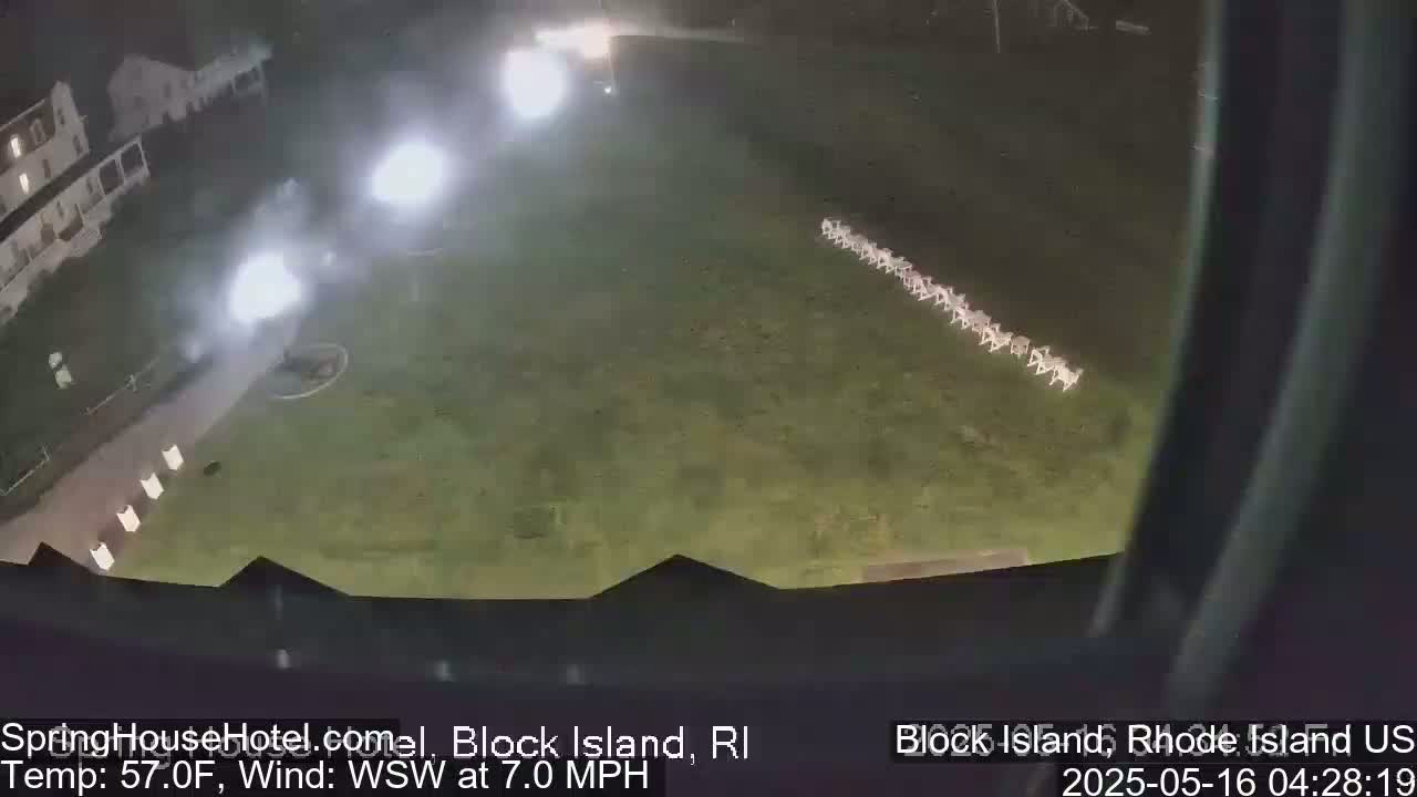 At night, under a WSW wind of 7 mph and a temperature of 57°F, a nighttime scene shows a building, bright lights, and a row of objects on a grassy field.