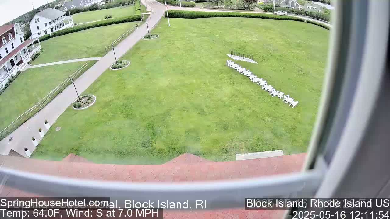 A view from a window shows a grassy area with a row of white chairs, a building, and a paved path; the weather is sunny with a 7 mph south wind and a temperature of 64°F.