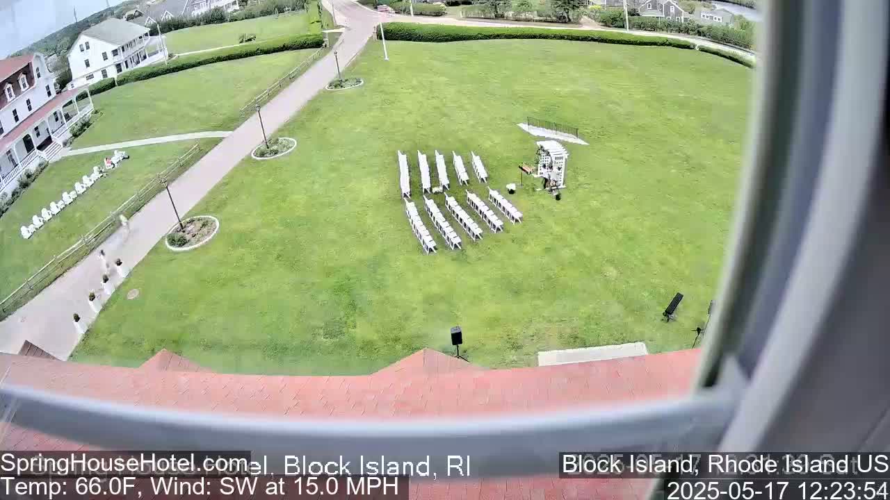 An outdoor wedding setup with white chairs arranged on a grassy lawn, under a partly sunny sky with a southwest wind at 15 mph.