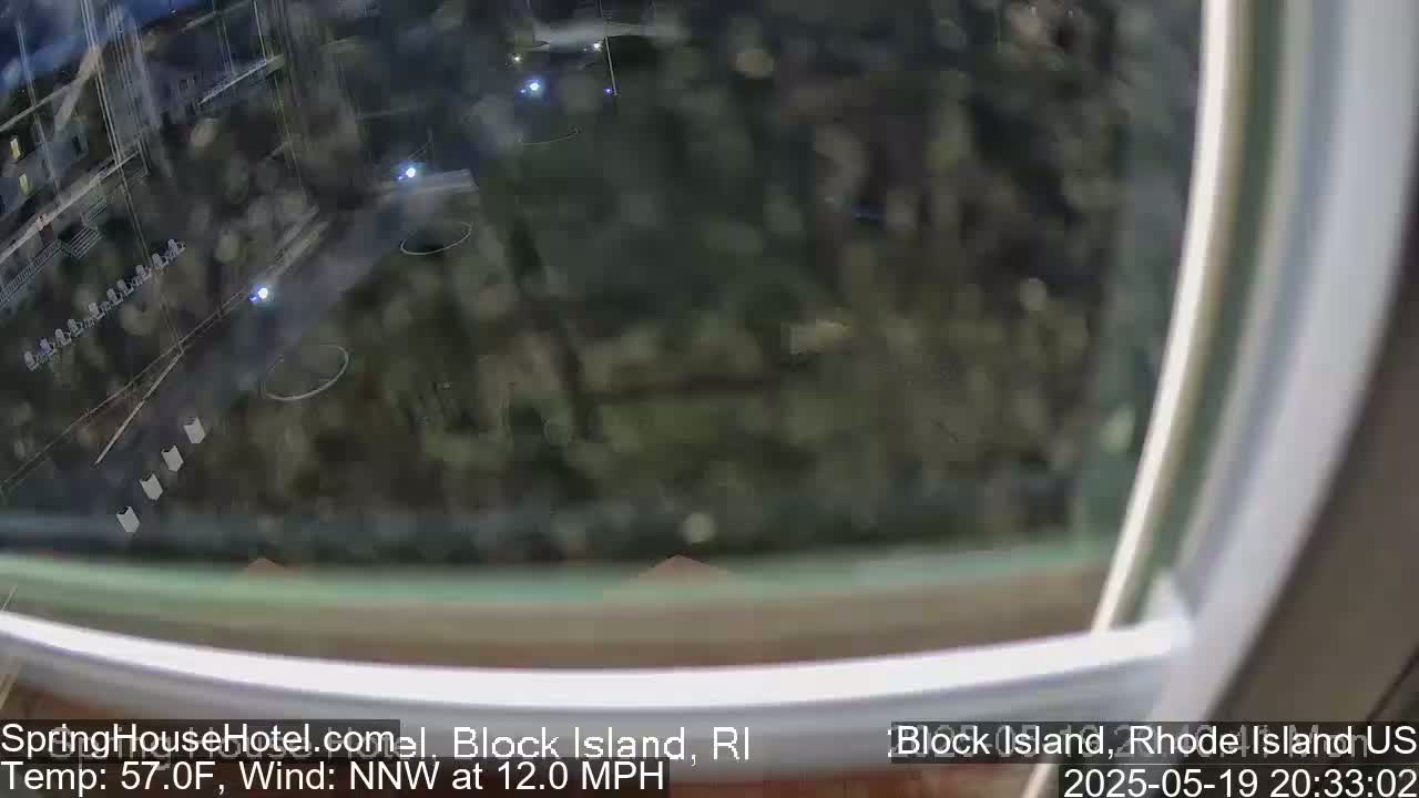 A nighttime view through a window shows a blurry, dark outdoor scene with some lights visible in the distance and a northwest wind at 12 mph.