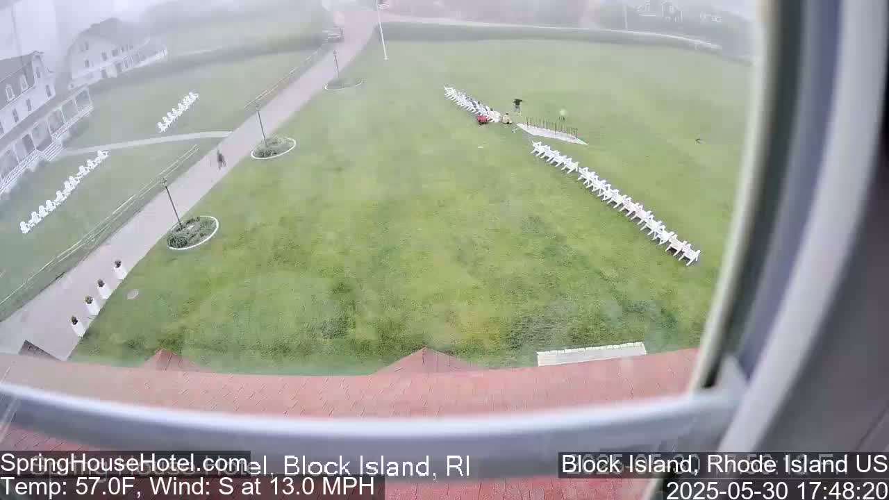 A foggy view from a window shows a grassy lawn with rows of white chairs, a building, and a person walking on a path.