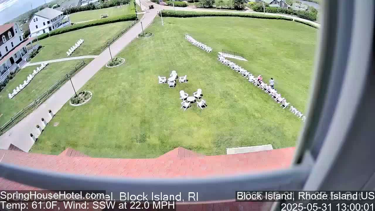 A grassy lawn with white chairs arranged in rows and small clusters, near a building, under sunny skies with a south-southwesterly wind blowing at 22 mph.