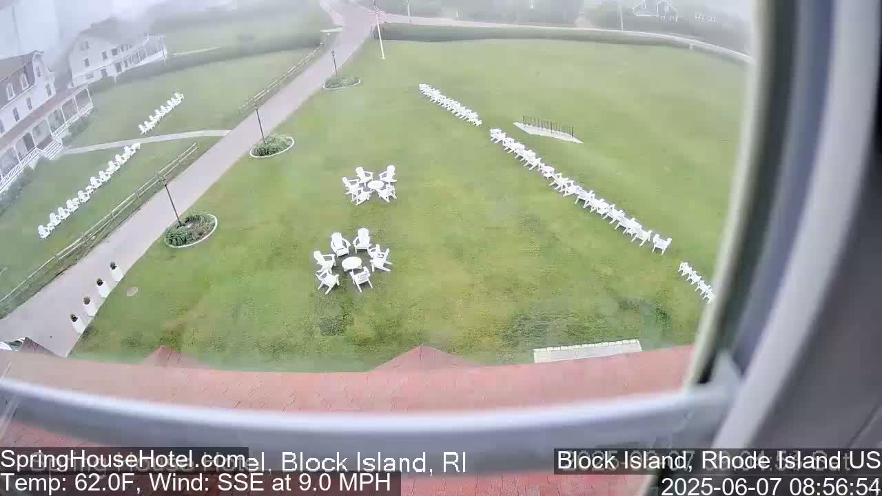 A grassy lawn with numerous white Adirondack chairs arranged in groups and lines, viewed from above in overcast conditions.