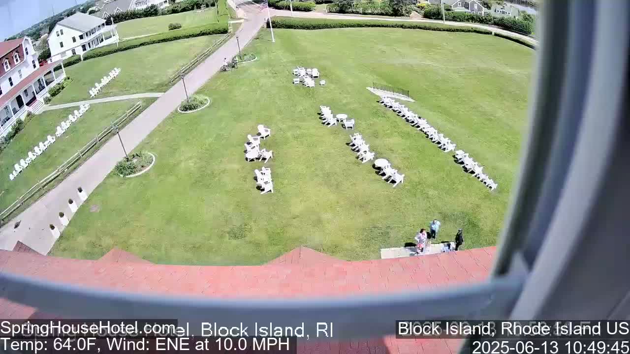 A grassy lawn with rows of white chairs and small tables, a building, and several people are visible on a sunny day with a 10 mph east-northeast wind.