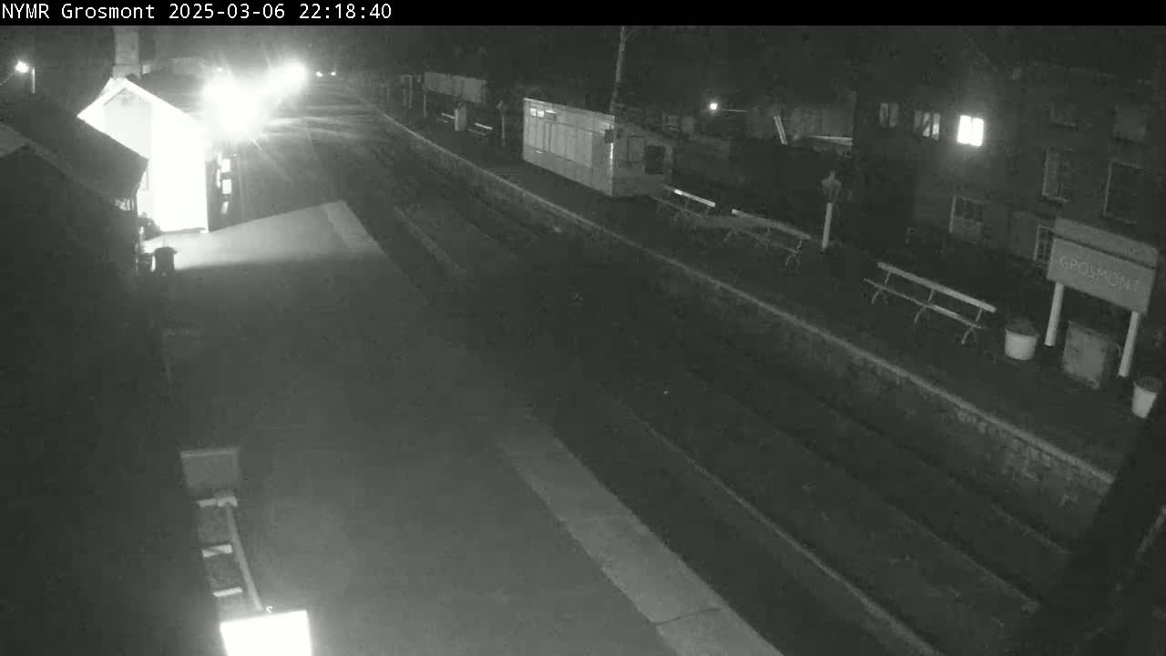 A nighttime view of a train platform with a building and benches, under dark conditions.