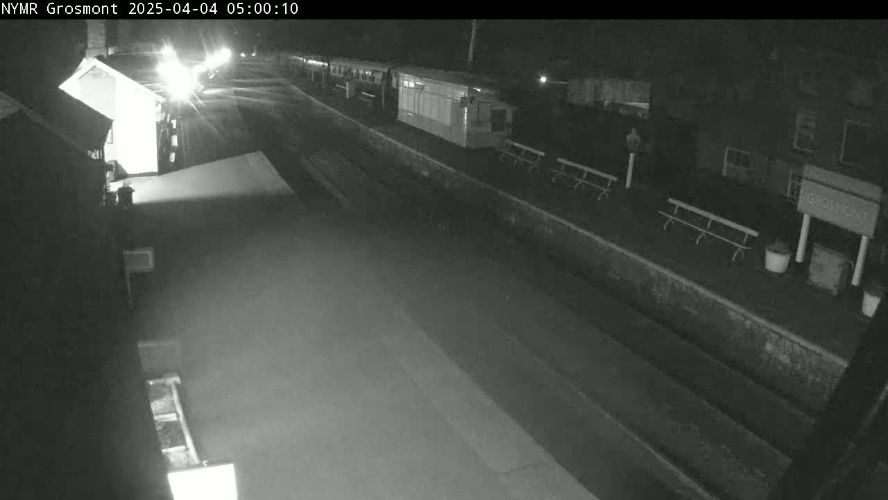 A nighttime, black and white view of a train at a deserted station platform.