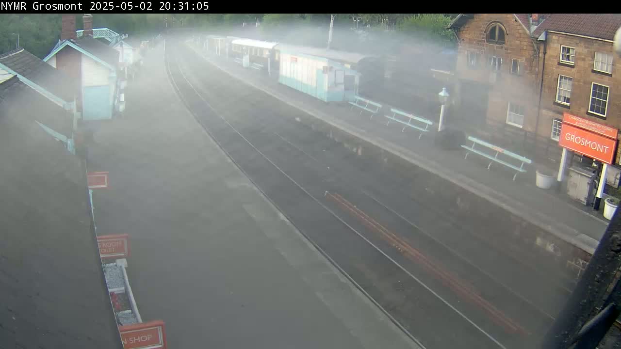 A foggy view of a train station platform with several buildings and benches.
