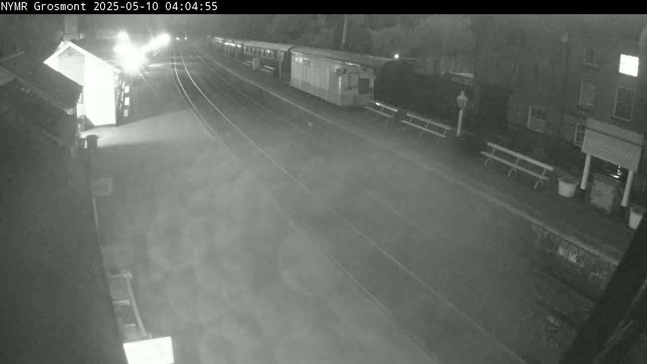 A nighttime, dimly lit train station platform with several train cars parked and a train approaching.