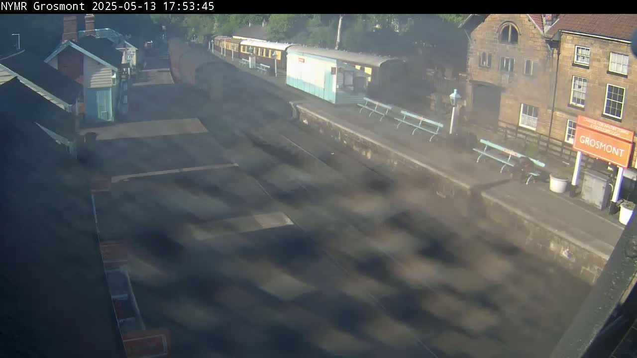 A hazy view of a train station with several passenger cars on the tracks and stone buildings nearby.