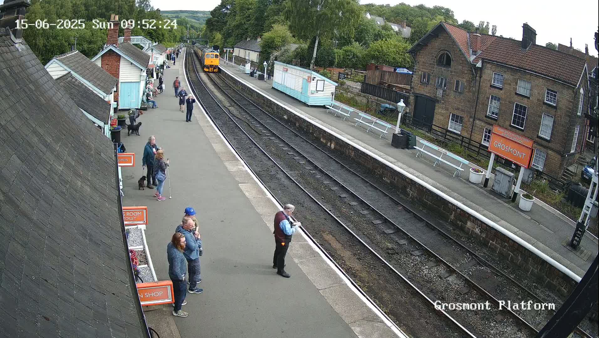 A train is arriving at a station platform on an overcast day, where several people are standing and watching.