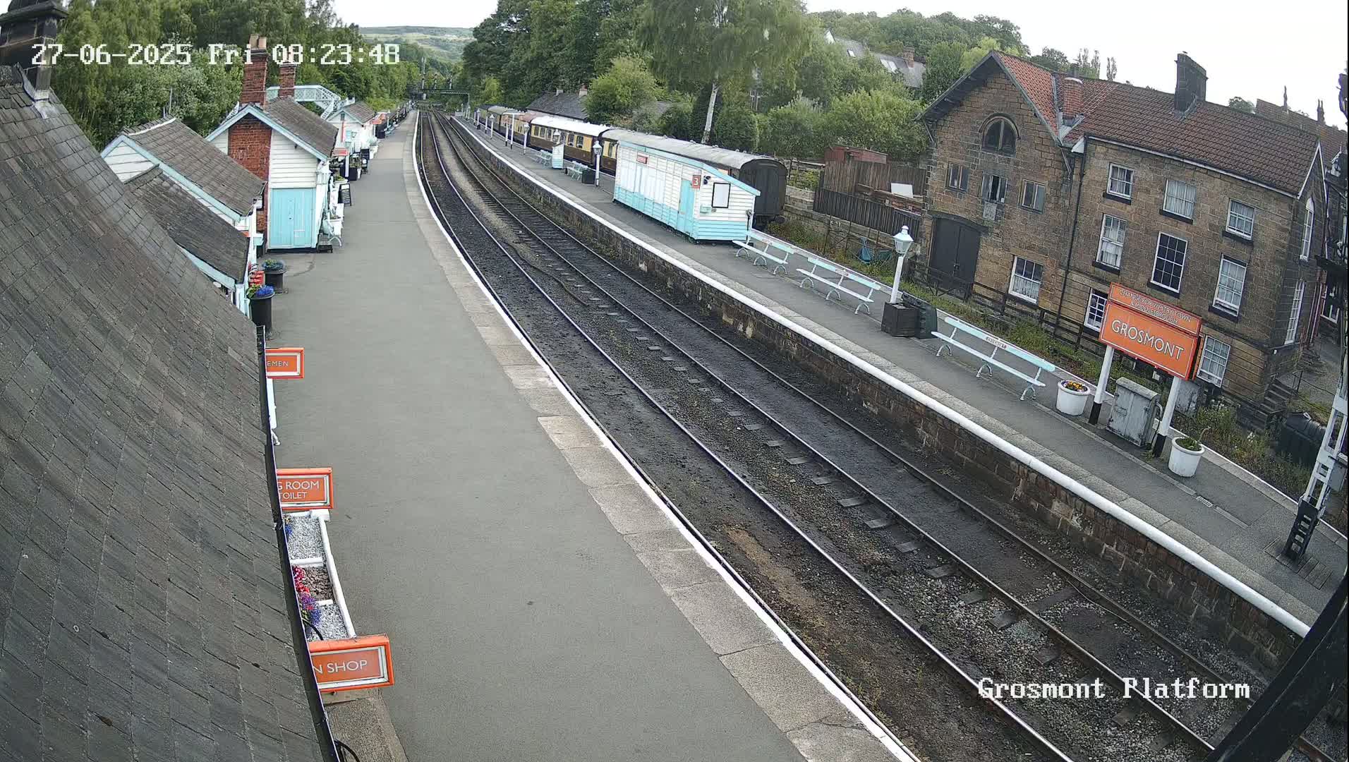 A railway platform with several train carriages, small buildings, and benches, under overcast skies.