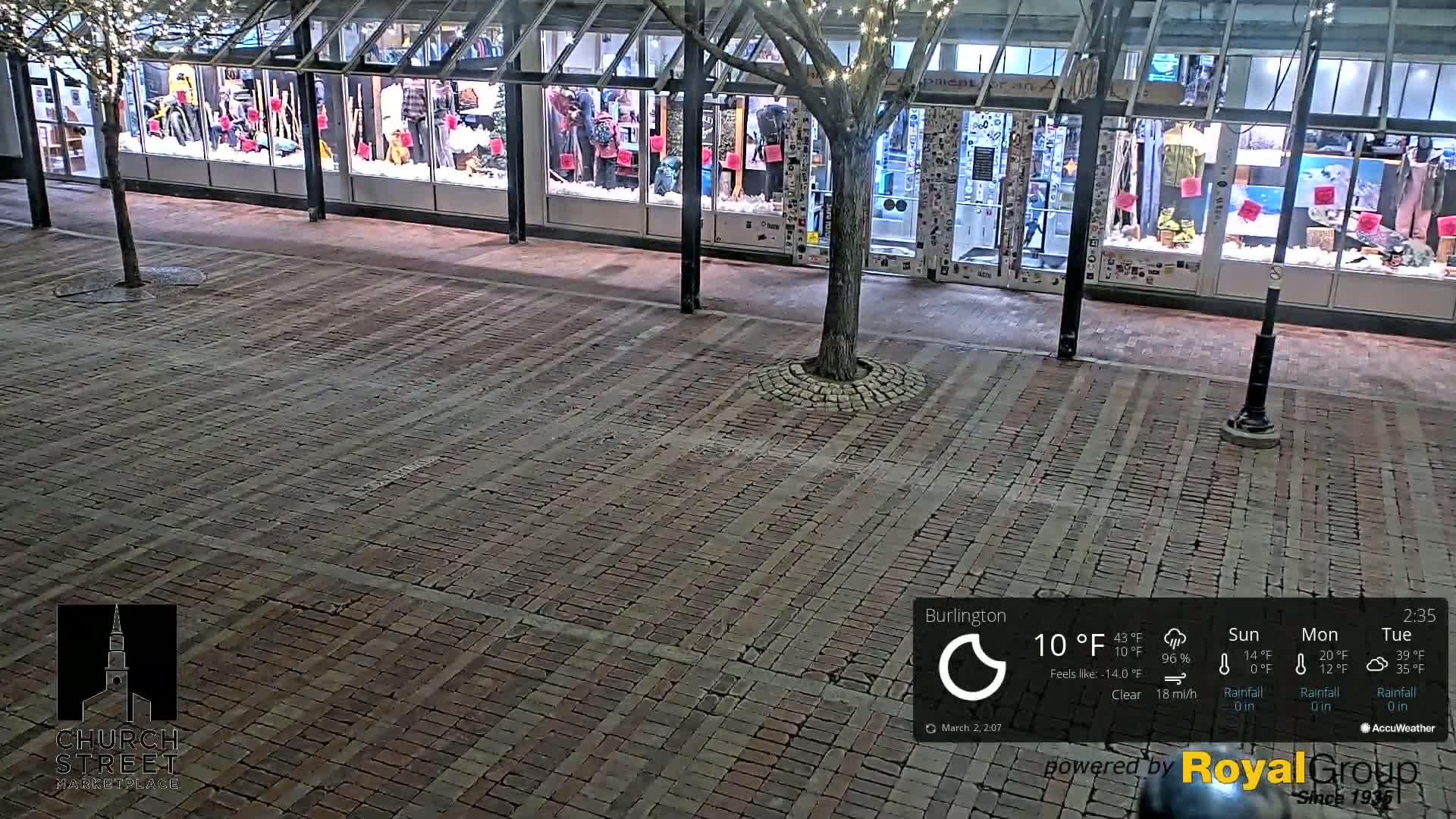 A brick-paved street at night, in front of a store with large windows displaying winter clothing, under a clear sky with a temperature of 10°F.