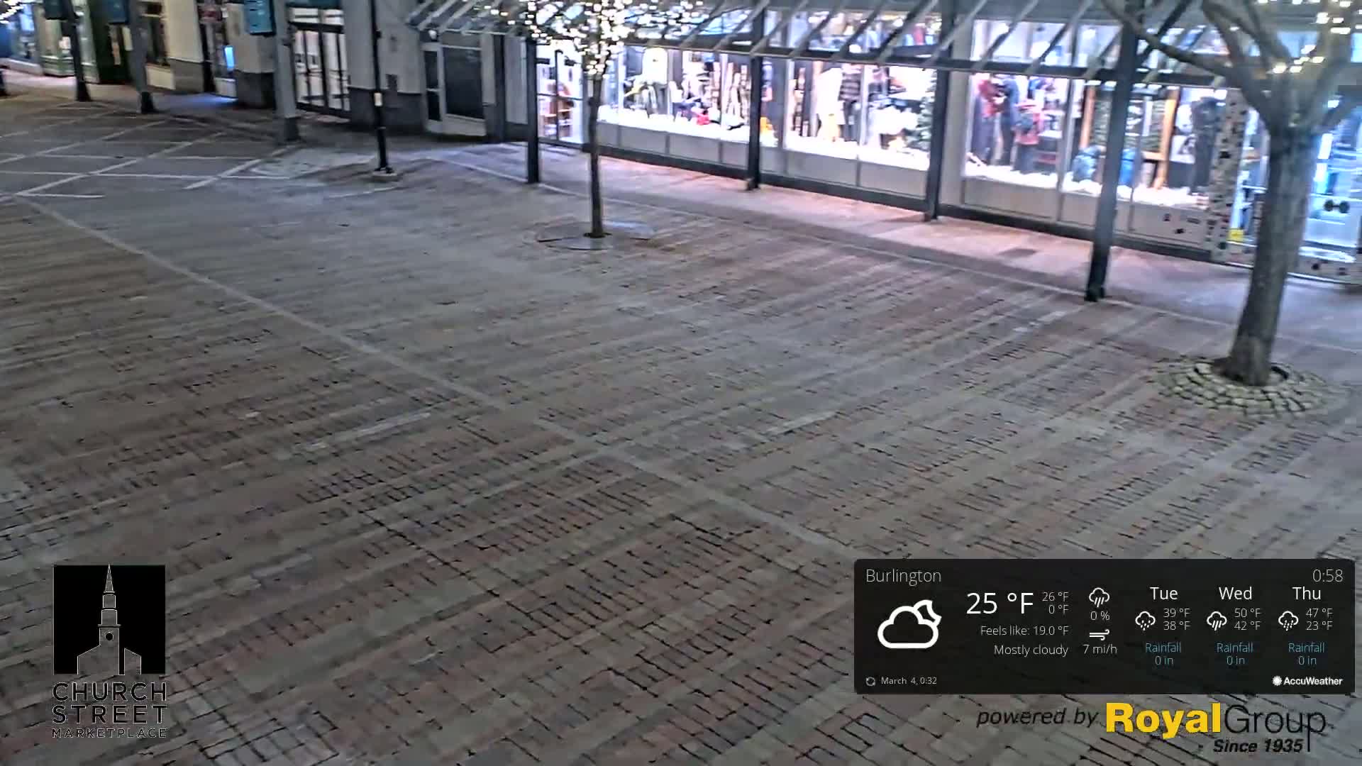 A mostly cloudy night scene shows an empty brick plaza in front of a storefront with minimal pedestrian activity.