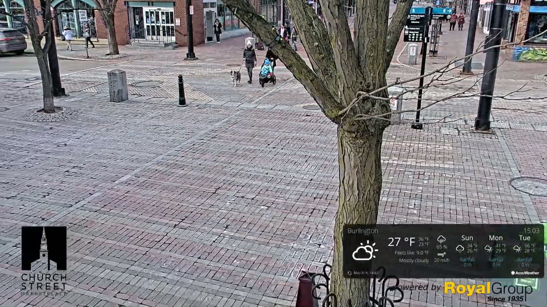 A mostly cloudy, 27°F day is shown over a brick paved street where two people are walking dogs and pushing a stroller.