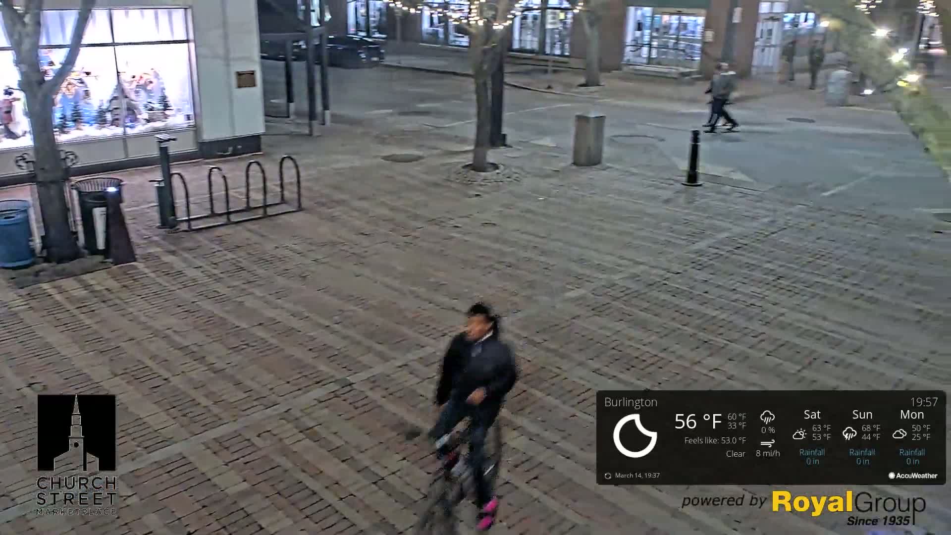 A person on a bicycle rides across a brick paved area at night under clear skies.